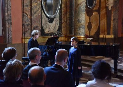 Adventní koncert ZUŠ 7.12.2019 - Klementinum. Pohled na paní klavíristku A. Barthovou a zpívající děvče.
