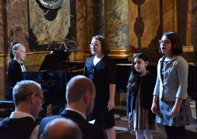 Adventní koncert ZUŠ 7.12.2019 - Klementinum. Pohled na děvče hrající na klavír a další tři zpívající děvčata.