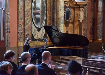 Adventní koncert ZUŠ 7.12.2019 - Klementinum. Pohled na publikum a hrající děvče na klavír.