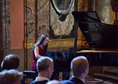Adventní koncert ZUŠ 7.12.2019 - Klementinum. Pohled na publikum a hrající děvče na klavír.