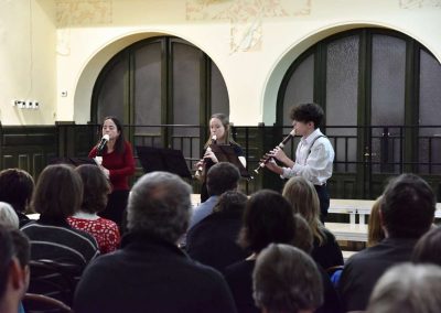 Adventní koncert přípravnýho pěveckýho sborů Pueri gaudentes 15.12.2019. Pohled na hrající flétnové trio - paní učitelka, děvče a kluk.