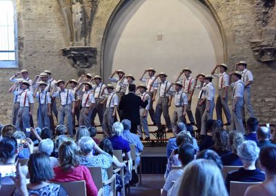 Závěrečný koncert Pueri gaudentes 24.6.2019 - Anežský klášter. Pohled na publikum, pana sbormistra L. Sládka a zpívající mužský sbor.