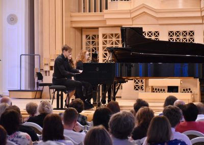 Slavnostní koncert ZUŠ Open, HAMU, 31.5.2020. Klavírní duo pro dva klavíri. Pohled na hrajícího chlapce a děvče.