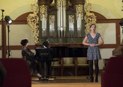 Pěvecký koncert, Profesní dům MFF, zpívající žačka a paní učitelka doprovázející na klavír.