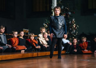 Vánoční koncert Pueri gaudentes, 19.12.2022, Betlémská kaple, Praha, zpívající chlapec a chlapecký sbor sedící na pódiu.