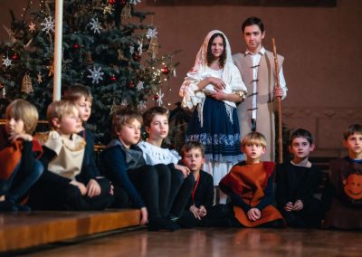 Vánoční koncert Pueri gaudentes, 19.12.2022, Betlémská kaple, Praha, chlapecký sbor sedící na pódiu a dva herci.