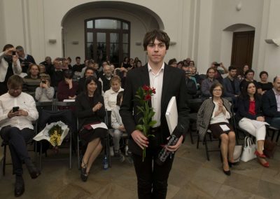 I. absolventský koncert, Atrium na Žižkově, 10.5.2023, absolvent s kytkou a vysvědčením a za ním publikum