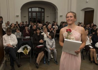 I. absolventský koncert, Atrium na Žižkově, 10.5.2023, absolventka s kytkou a vysvědčením a za ní publikum